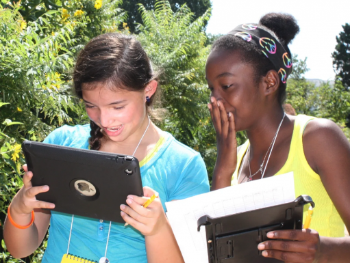 Two girls look at data on a digital device in the field. 